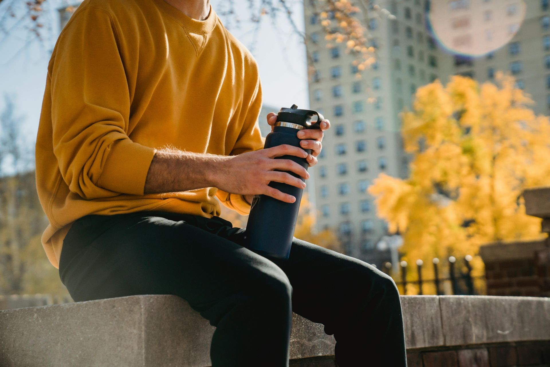 Man waring an orange jumper sat on a wall holding a black water bottle