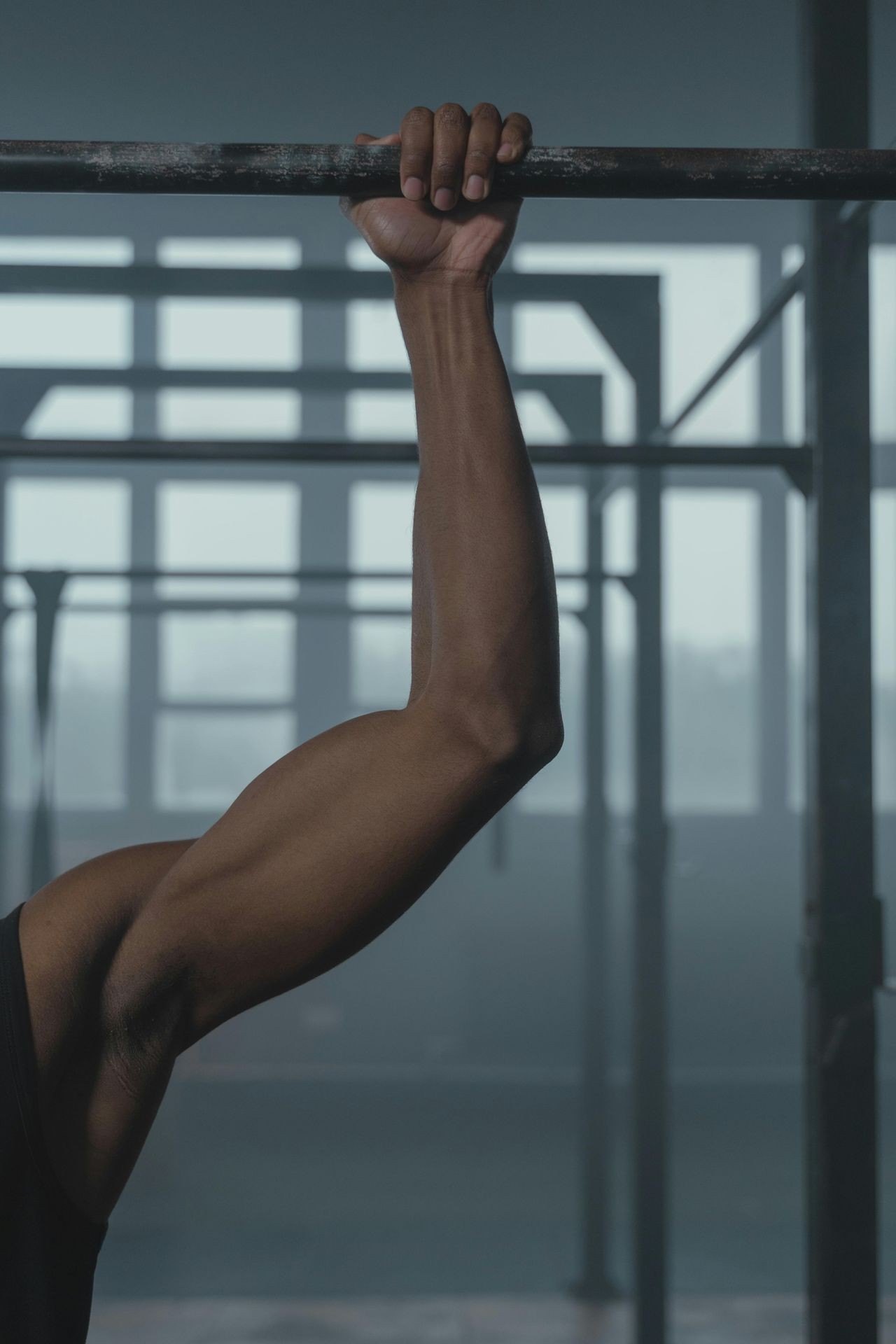 A muscular guys arm beneath a pullup bar