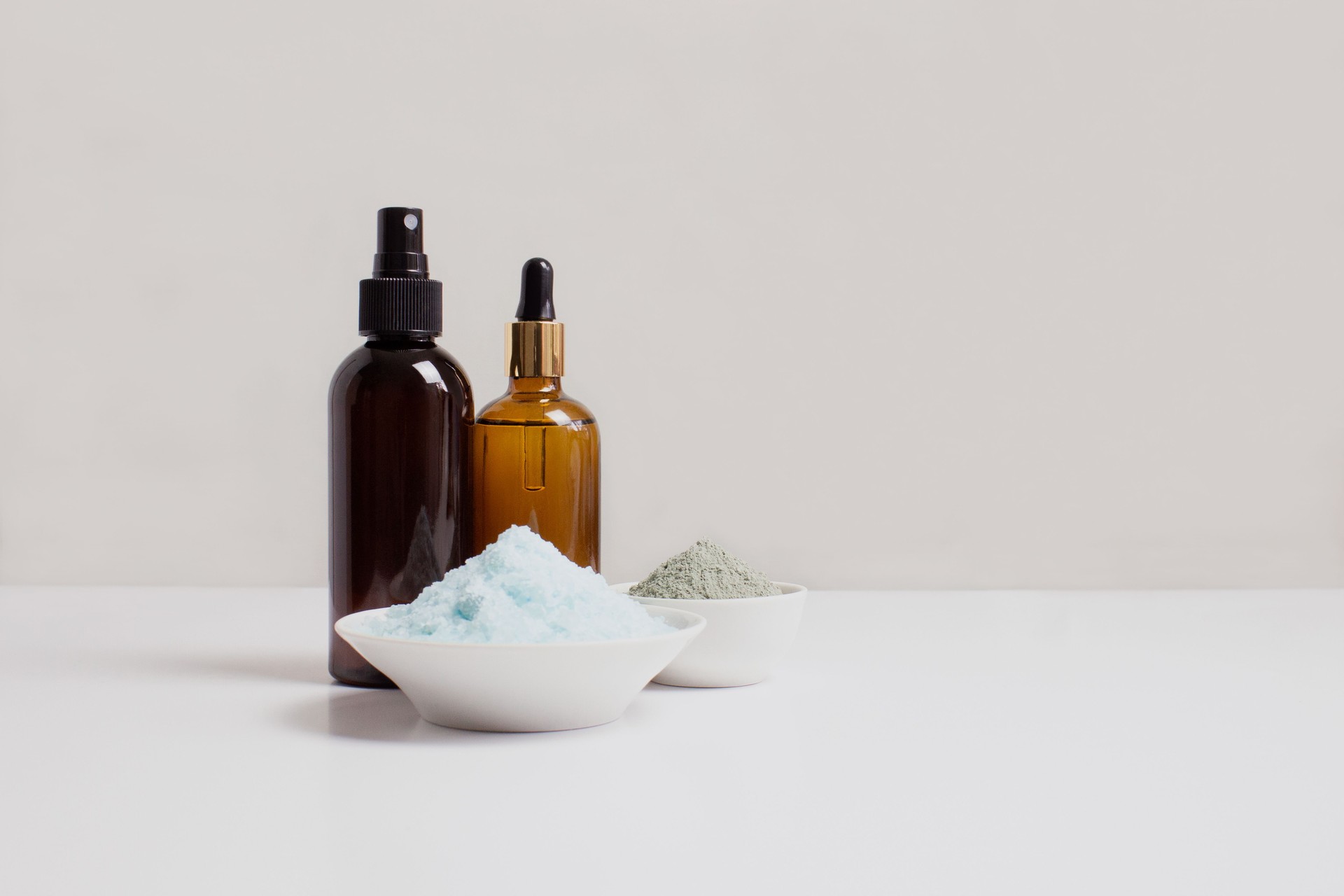 Sea salt, serum in brown dropper glass and spray bottle, clay for hair and face, beige background side view. Organic, natural cosmetic. Skincare, spa.