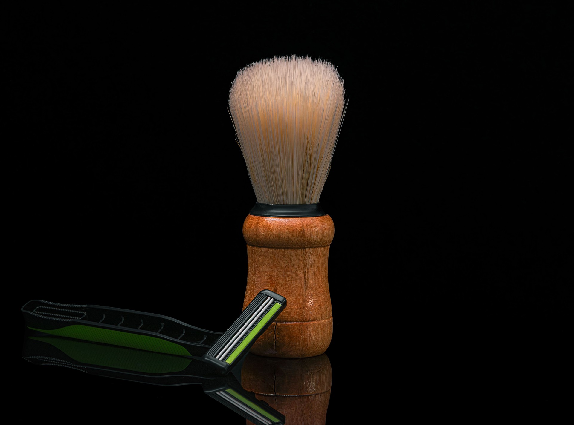 Shaving brush and razor on a dark background and subtle reflection.
