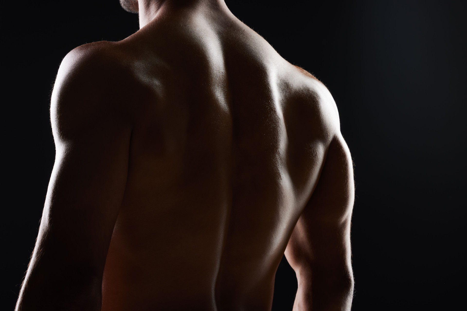 Man, back and muscle with silhouette, studio and shadow for wellness, health and strong by black background. Bodybuilder guy, shirtless and fitness with skin, aesthetic and power in dark for art